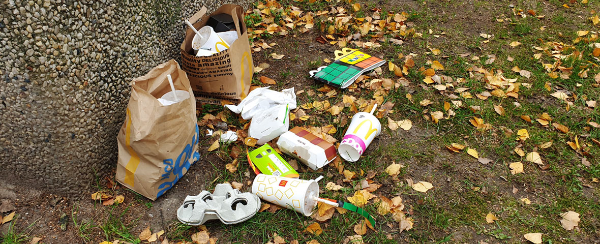 Foto: Papiertragetaschen, leere Verpackungen und Essensreste vor eine Müllbox geworfen